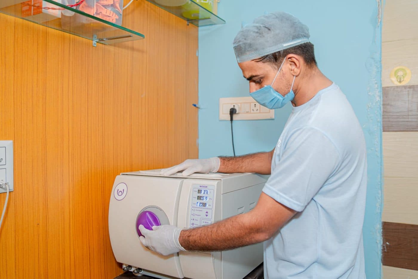 A team member in a mask and cap loading the autoclave in the sterilisation room